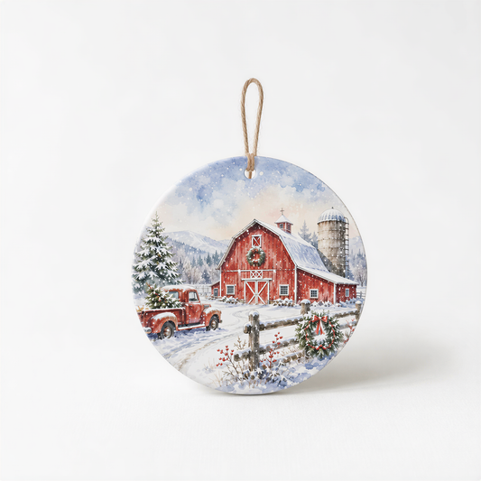 A round ornament depicting a red barn with a Christmas tree in front, a truck parked in front of the barn, and a wreath on the fence.