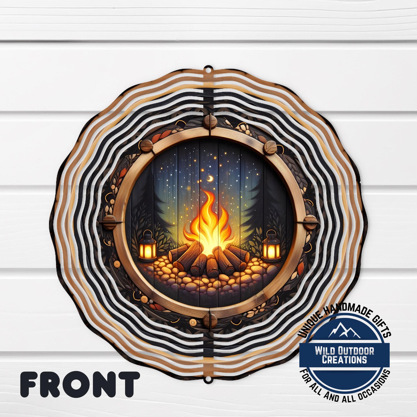 a decorative metal piece with a circular design, depicting a campfire surrounded by a forest scene.