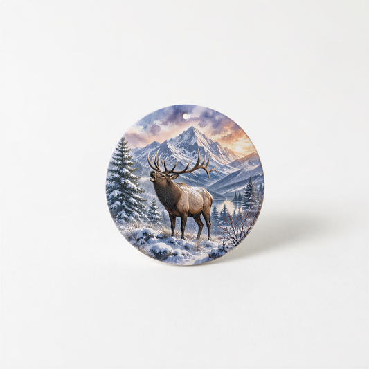 A deer with large antlers stands in a snowy mountain landscape, with a pine tree and a mountain range in the background.