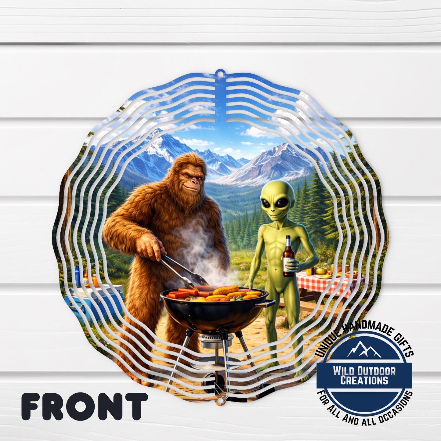 A large metal sculpture depicting a giant brown furry creature cooking food on a grill, with a smaller alien-like creature standing nearby. The sculpture is set against a backdrop of mountains and a clear blue sky.