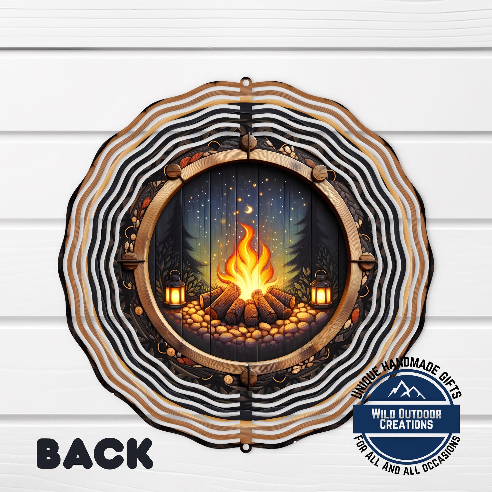 a decorative metal piece with a circular design, depicting a campfire surrounded by a forest scene.